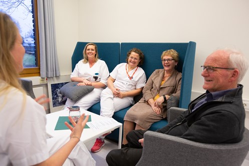 Pasient og pårørende sitter i sofagruppe sammen med lege og sykepleiere
